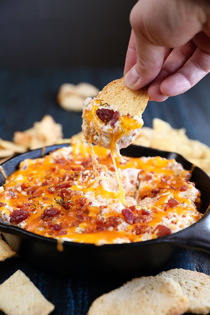 Cheesy Chicken Bacon Ranch Dip scooping out of  pan with a chip